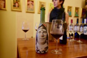 Bottle of wine with a wine glass next to it and a woman looking on.