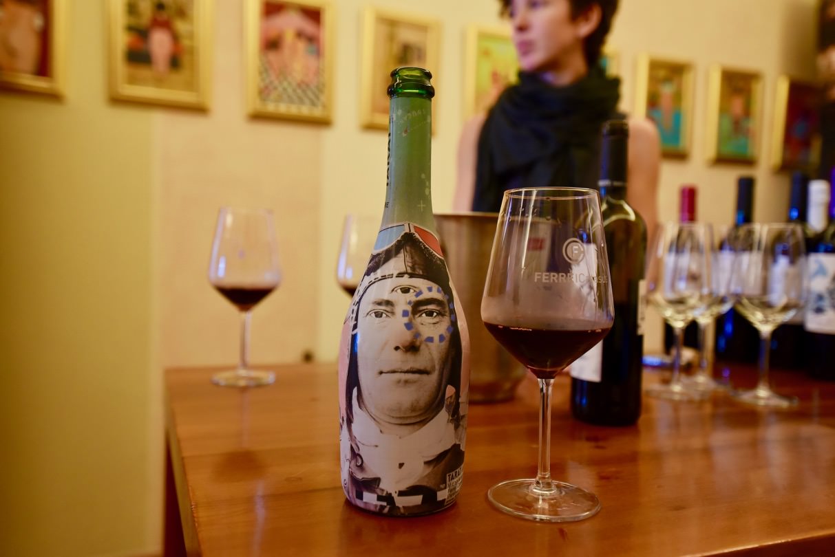 Bottle of wine with a wine glass next to it and a woman looking on.