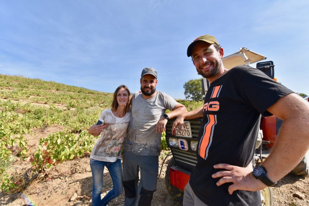 Two men and a woman standing next to a tractor in a vineyard.