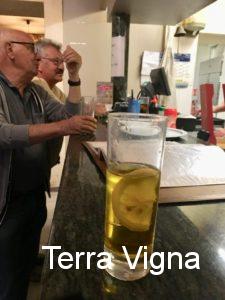 two men standing at the bar with a glass of yellow drink.