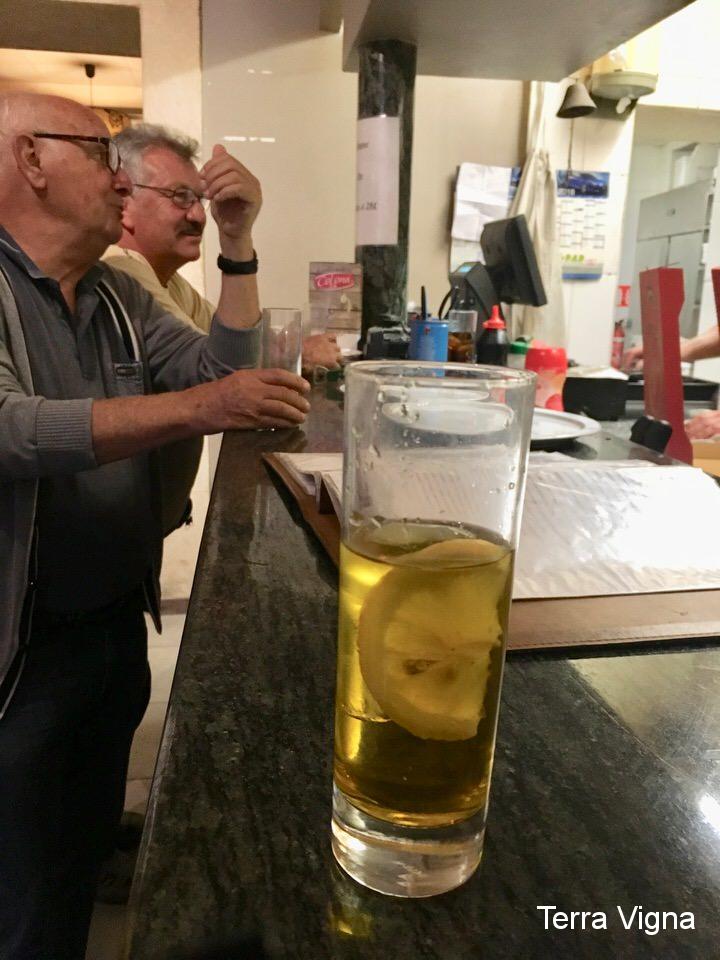 two men standing at the bar with a glass of yellow drink.