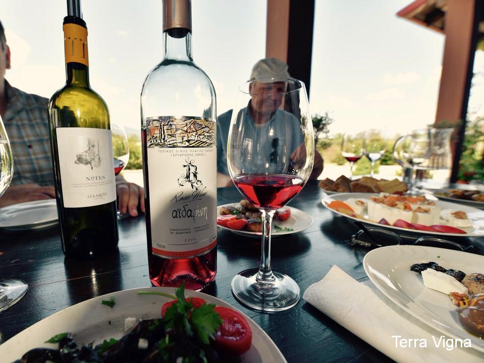 Two bottles of wine on a table next to a glass of Aidarini rose of Xinomavro.