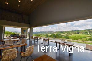 A room with tables and chairs with the view of wineries from the windows.