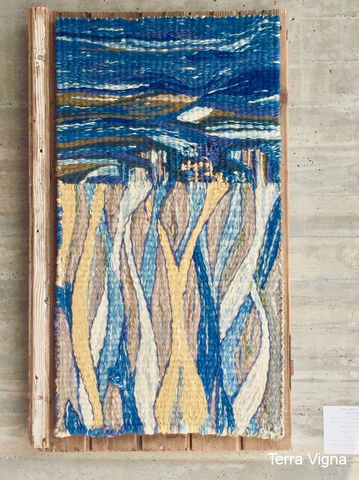 A loom made weave art work hanging on a wall.