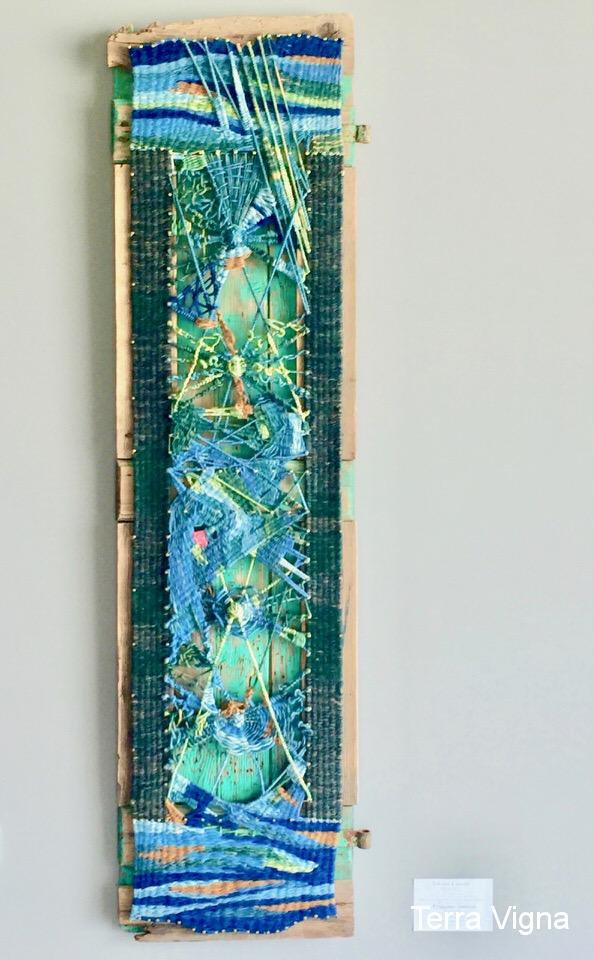 A loom made weave art work hanging on a wall.