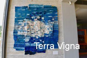 A blue loom made weave art work hanging on a wall.