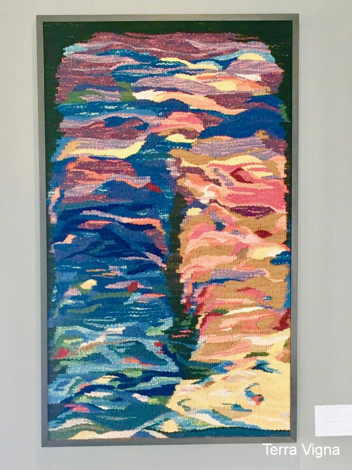 A loom made weave art work hanging on a wall.