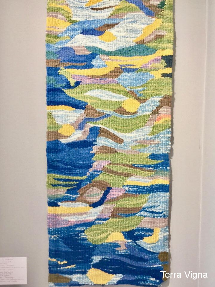 A loom made weave art work hanging on a wall.