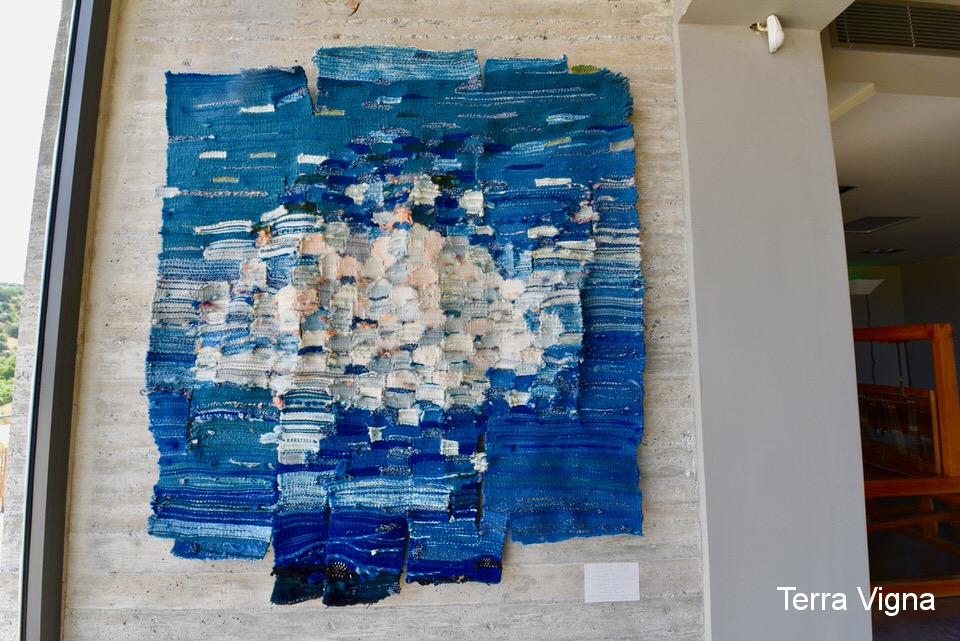 A blue loom made weave art work hanging on a wall.