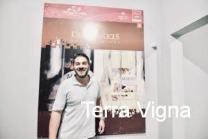 A man standing in front of a large poster of Digenakis Winery.