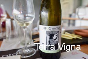 A bottle of Greek white wine next to a glass of white wine.