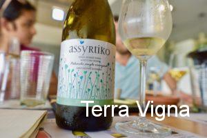 A bottle of white Greek wine on a table next to a glass of wine.